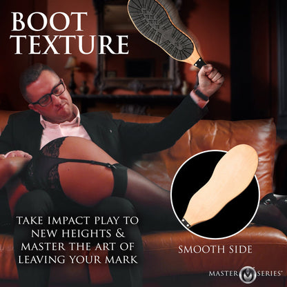 A BDSM paddle with a rugged black rubber boot sole on one side and smooth polished wood on the other, featuring a vegan leather-wrapped handle and hanging loop.

