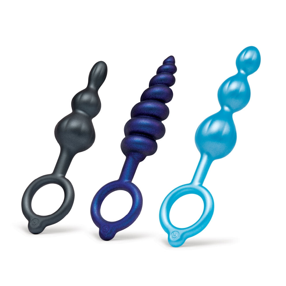 A set of three graduated silicone anal plugs in varying textures and sizes, featuring smooth, beaded designs in black, blue, and metallic purple. Each plug has a retrieval ring for easy handling and removal, and the plugs are displayed upright to highlight their unique shapes.