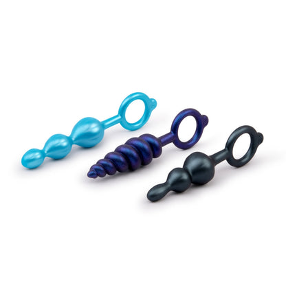 A set of three graduated silicone anal plugs in varying textures and sizes, featuring smooth, beaded designs in black, blue, and metallic purple. Each plug has a retrieval ring for easy handling and removal, and the plugs are displayed upright to highlight their unique shapes.