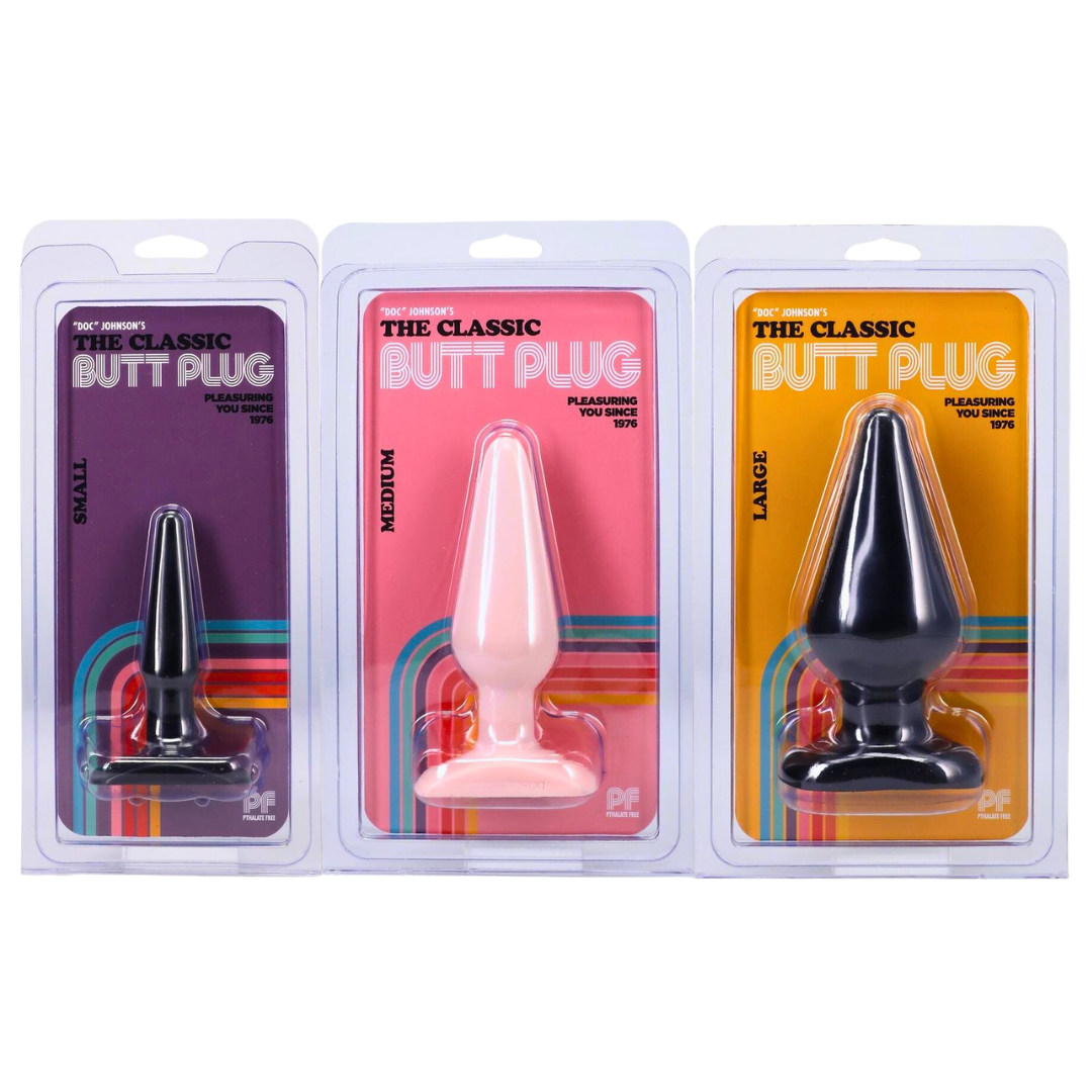 Packaging of Doc Johnson's The Classic Butt Plug in small, medium, and large sizes. Each size is displayed in vibrant retro-themed packaging, highlighting its tear-drop shape and flared base. Available in black and white, labeled as "Pleasuring You Since 1976."