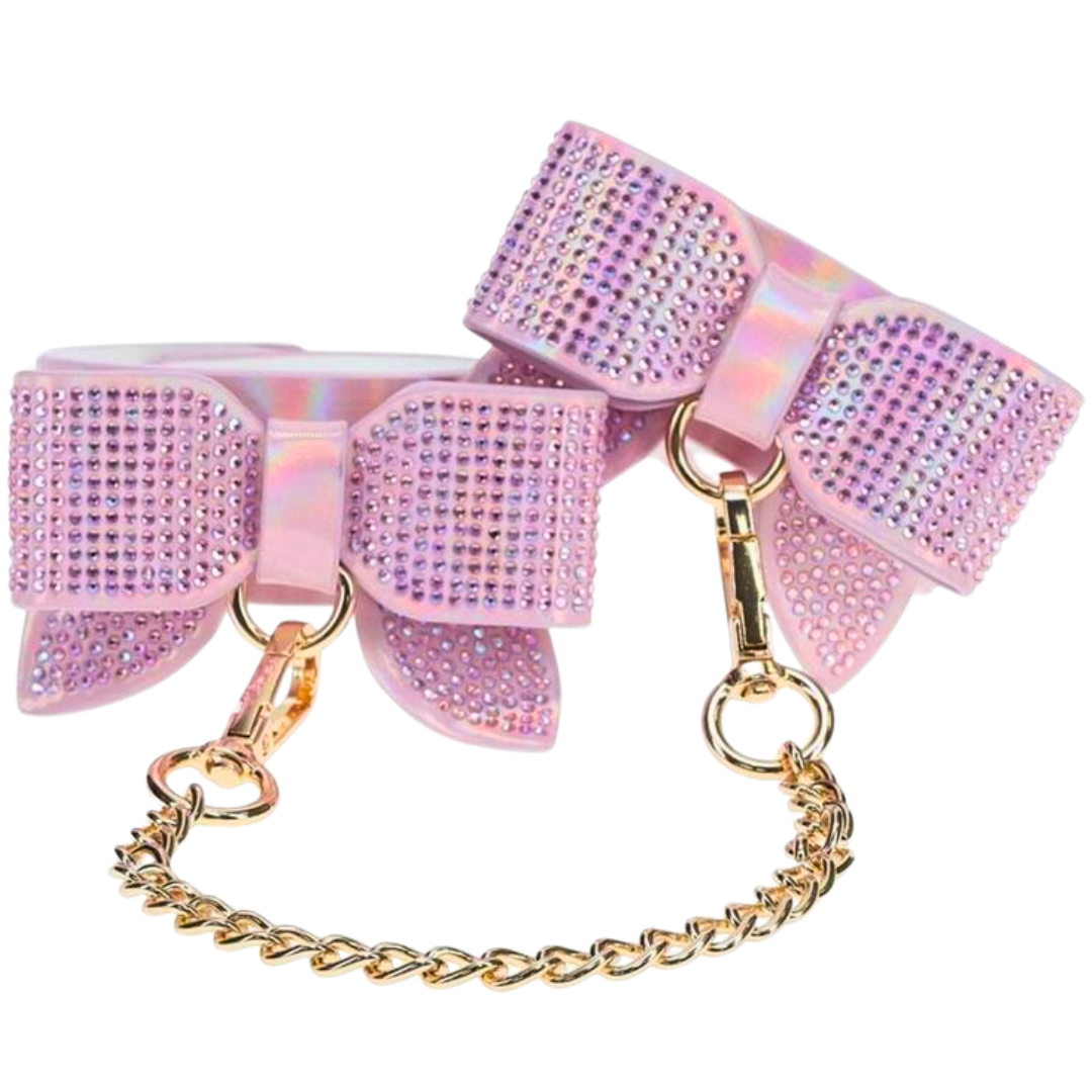 Adjustable ankle cuffs with rhinestone bows and gold chain leash, available in iridescent black, pink, and blue for stylish BDSM play.