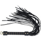 a black flogger, a BDSM accessory designed for impact play. The handle is sturdy and wrapped in black material with gold accents, offering a secure grip. The flogger features multiple soft leather strands, making it suitable for a range of sensations, from light teasing to more intense impact. At the base of the handle, there is a metallic loop for hanging or easy storage. The overall design is sleek and elegant, combining functionality with a stylish aesthetic. London Collection Flogger by Ouch! featuring 